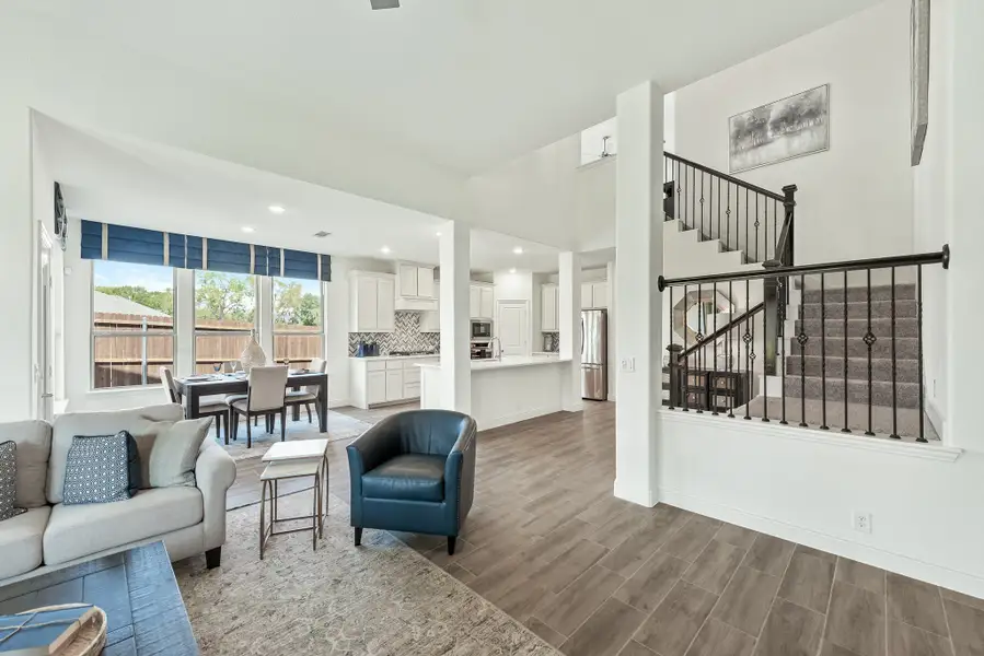 Open-concept living area with hardwood floors, staircase with iron railings, and kitchen visible in background