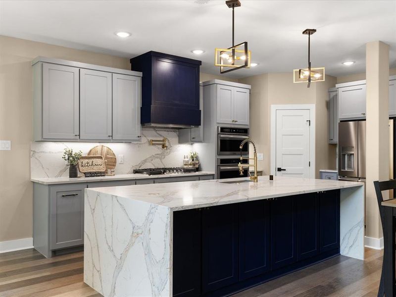 Kitchen featuring light stone countertops, backsplash, gray cabinetry, dark wood finished floors, and a center island with sink