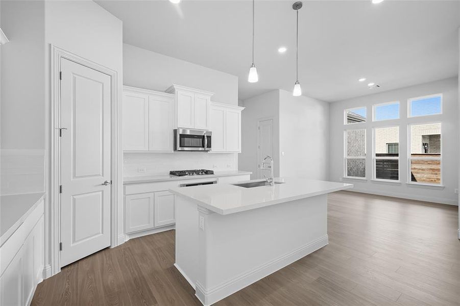 Kitchen featuring white cabinets, a kitchen island with sink, light wood-style floors, decorative light fixtures, and recessed lighting