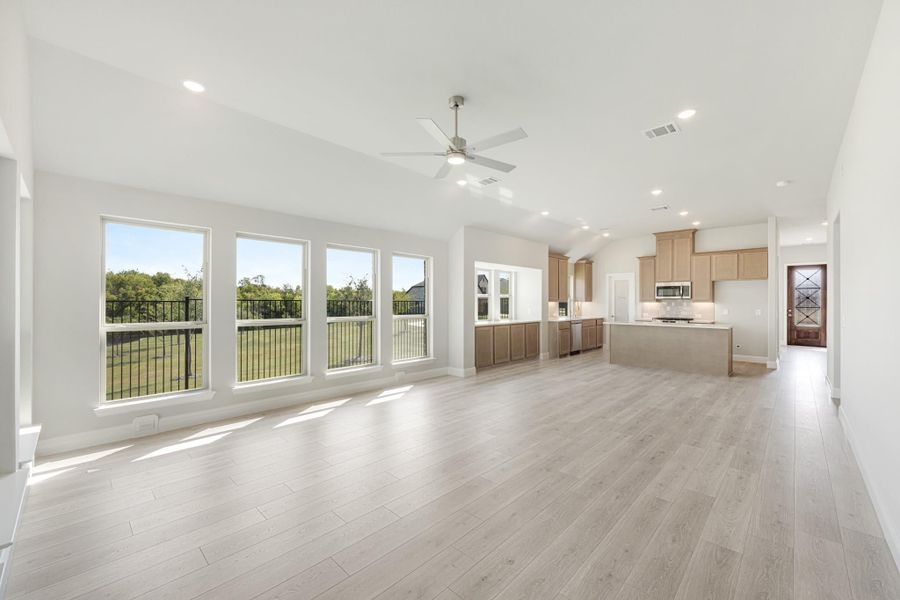 Open-plan living area with light wood floors, ceiling fan, and kitchen with island visible in background