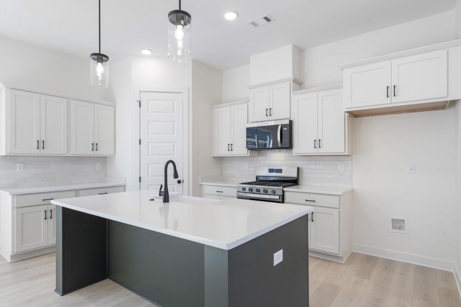 Kitchen featuring white cabinetry, a contrasting dark-toned center island with a stone-finish countertop, subway tile backsplash, stainless steel appliances, and two pendant lights Kitchen featuring white cabinetry, a contrasting dark-toned center island with a stone-finish countertop, subway tile backsplash, stainless steel appliances, and two pendant lights