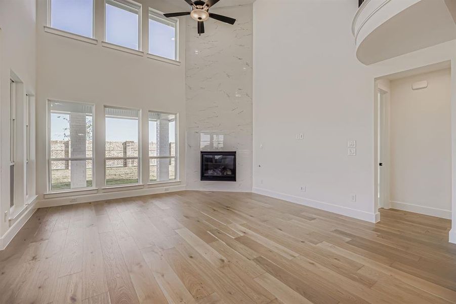 Unfurnished living room featuring a towering ceiling, light wood-type flooring, a high end fireplace, and ceiling fan