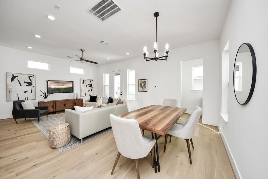 This photo showcases a modern open-concept living and dining area with light wood flooring and white walls. The space is bright, featuring a dining table with upholstered chairs, a comfortable seating area with a sofa and armchairs, and contemporary decor. Large windows and a glass door allow for ample natural light. This photo showcases a modern open-concept living and dining area with light wood flooring and white walls. The space is bright, featuring a dining table with upholstered chairs, a comfortable seating area with a sofa and armchairs, and contemporary decor. Large windows and a glass door allow for ample natural light.