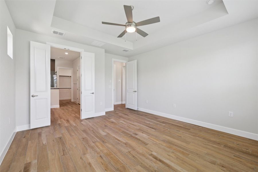 Unfurnished bedroom featuring a tray ceiling, light wood-type flooring, and ceiling fan