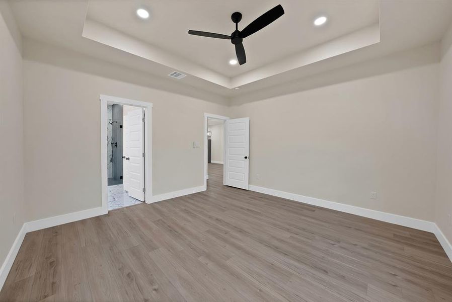 Unfurnished bedroom with a tray ceiling, light wood-style flooring, ceiling fan, and recessed lighting