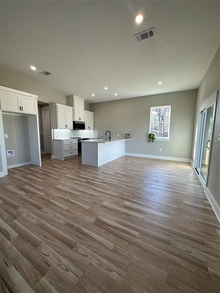 Kitchen with light hardwood / wood-style flooring, white cabinetry, tasteful backsplash, sink, and a center island with sink