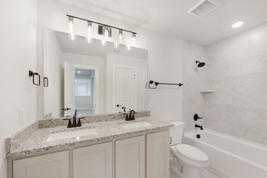 Bathroom with double vanity, granite countertop, white cabinets, and tiled shower-tub combo with dark bronze fixtures