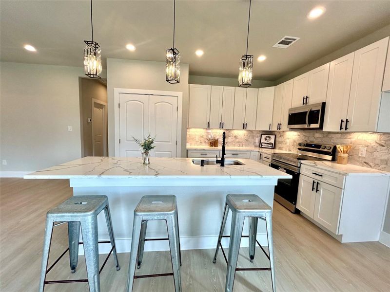 Kitchen with appliances with stainless steel finishes, white cabinets, hanging light fixtures, a kitchen bar, and light wood finished floors