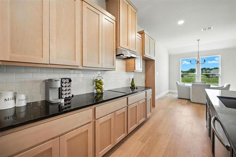 Kitchen featuring dark stone counters, light wood finish cabinets, light wood-style floors, dishwasher, and suspended lighting