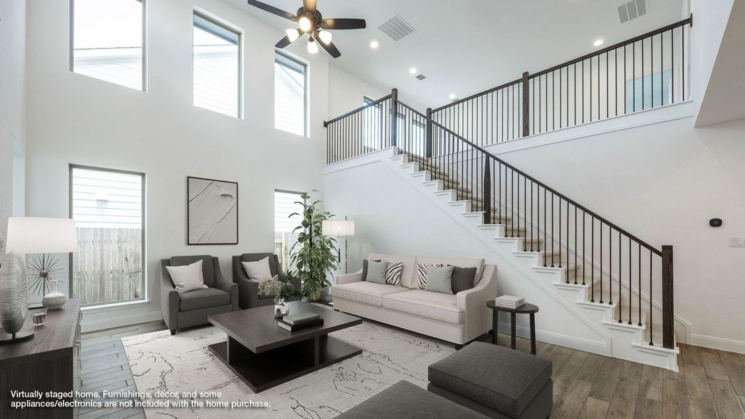 Living room featuring wood-type flooring, a towering ceiling, plenty of natural light, stairs, and a ceiling fan Living room featuring wood-type flooring, a towering ceiling, plenty of natural light, stairs, and a ceiling fan