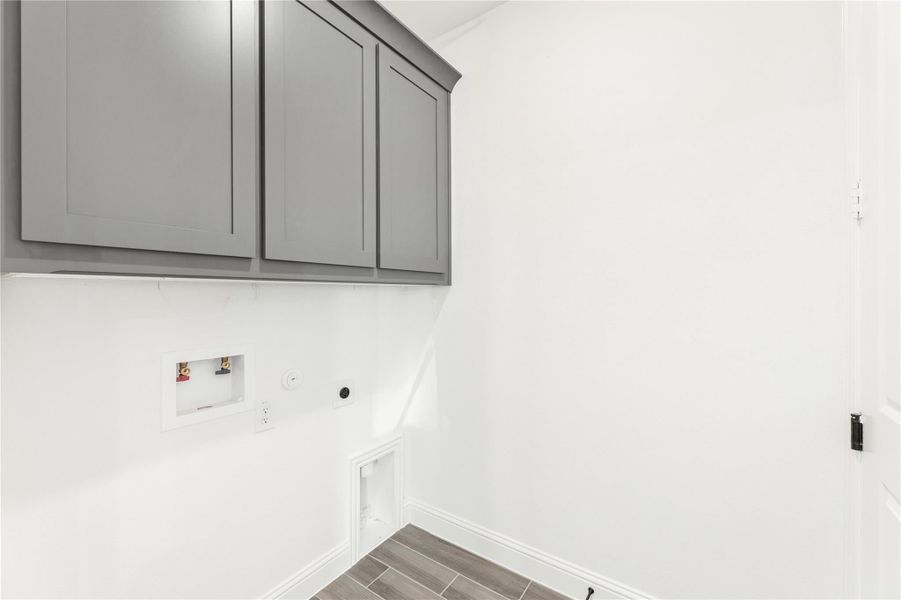 Laundry room with gray upper cabinets, washer and dryer hookups, and wood-look tile floor Laundry room with gray upper cabinets, washer and dryer hookups, and wood-look tile floor