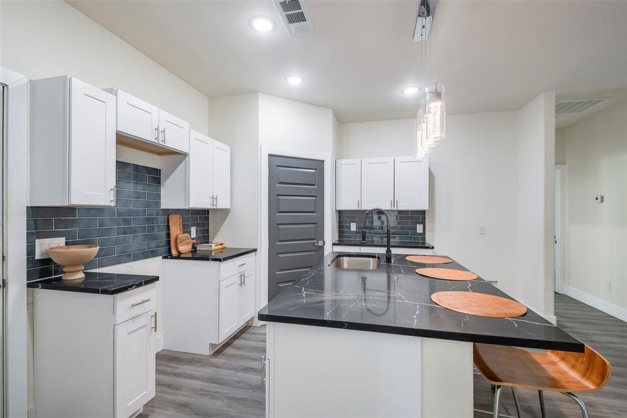 Kitchen featuring white cabinets, tasteful backsplash, decorative light fixtures, and hardwood / wood-style floors