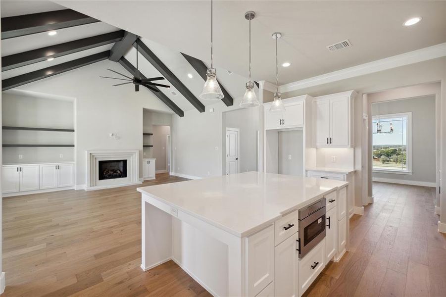 Kitchen featuring vaulted ceiling with beams, a kitchen island, white cabinets, stainless steel microwave, and light hardwood / wood-style flooring