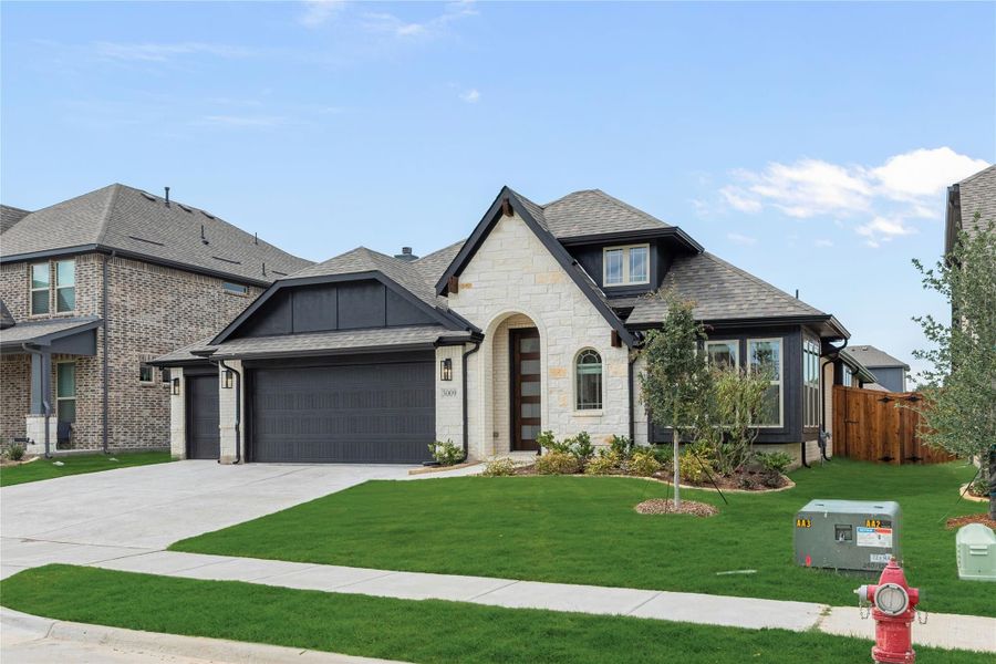 Single-story home with white stone exterior, dark trim, two-car garage, and landscaped front yard