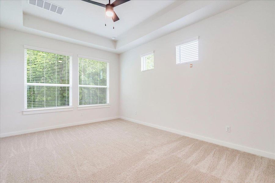 A well-proportioned bedroom with tray ceilings and abundant natural light invites comfortable living.