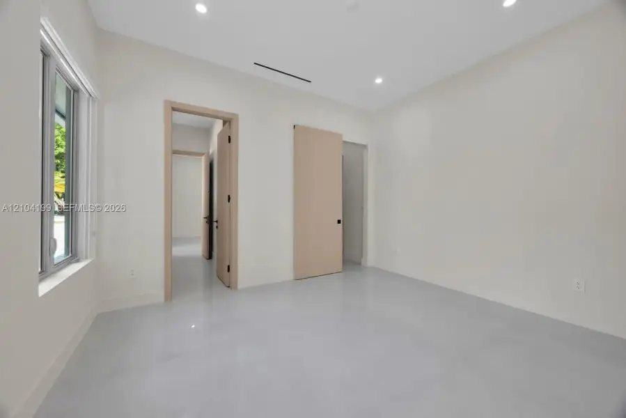 Neutral-toned room featuring smooth concrete-finish flooring, recessed lighting, light-wood interior doors, and a sliding barn-style door