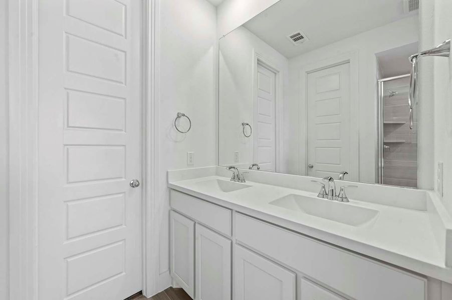 The primary bathroom showcases elegant white cabinetry, double sinks, and a large mirror that enhances its bright, sophisticated feel.