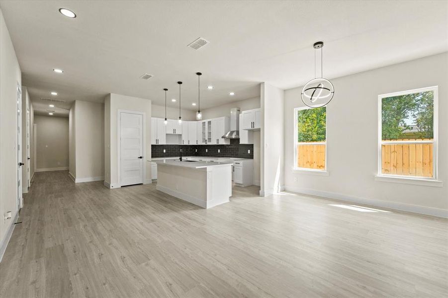 Kitchen featuring white cabinetry, decorative backsplash, glass insert cabinets, a center island with sink, and decorative light fixtures Kitchen featuring white cabinetry, decorative backsplash, glass insert cabinets, a center island with sink, and decorative light fixtures