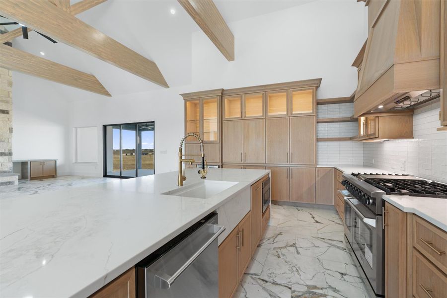 Kitchen with stainless steel appliances, open shelves, glass insert cabinets, light stone countertops, and high vaulted ceiling
