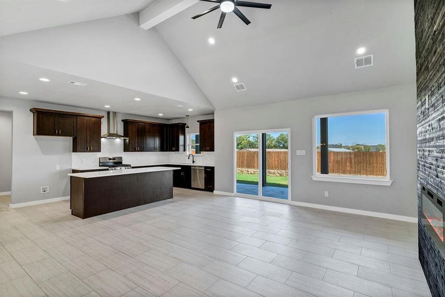 Kitchen featuring wall chimney exhaust hood, stainless steel appliances, ceiling fan, high vaulted ceiling, and a center island