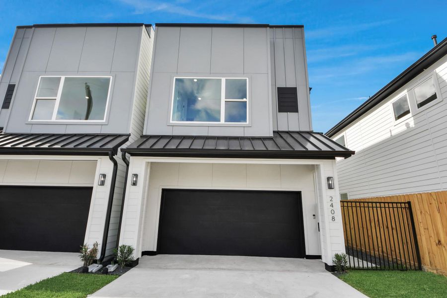 Modern townhouse with a sleek design, featuring a two-story facade and a black garage door. The exterior is complemented by large windows for natural light and a neatly fenced side yard.
