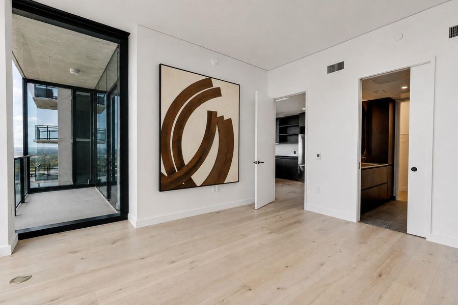 Floor-to-ceiling glass doors open to a private balcony from this modern space with light hardwood flooring. Floor-to-ceiling glass doors open to a private balcony from this modern space with light hardwood flooring.
