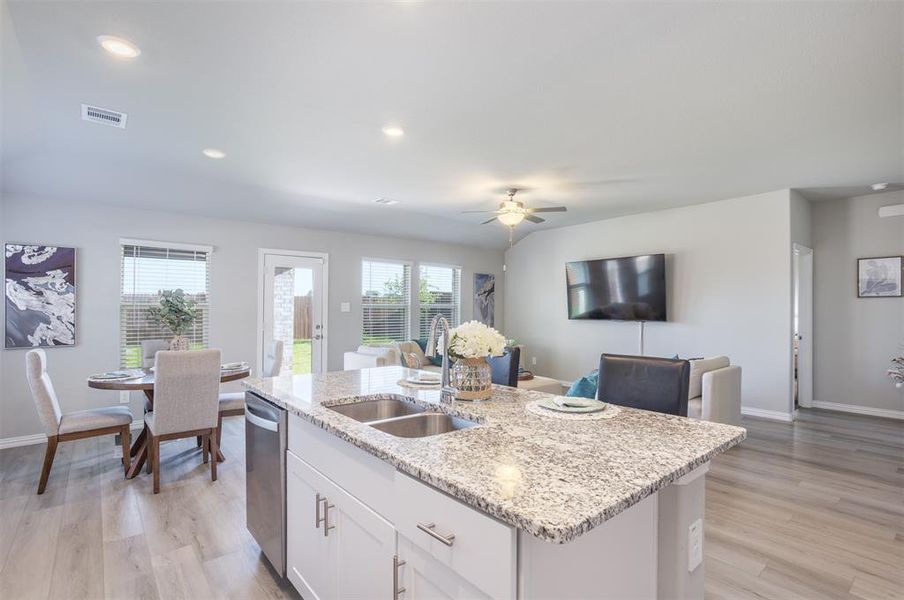 Kitchen featuring stainless steel dishwasher, a center island with sink, light wood-style flooring, white cabinets, and light stone counters Kitchen featuring stainless steel dishwasher, a center island with sink, light wood-style flooring, white cabinets, and light stone counters