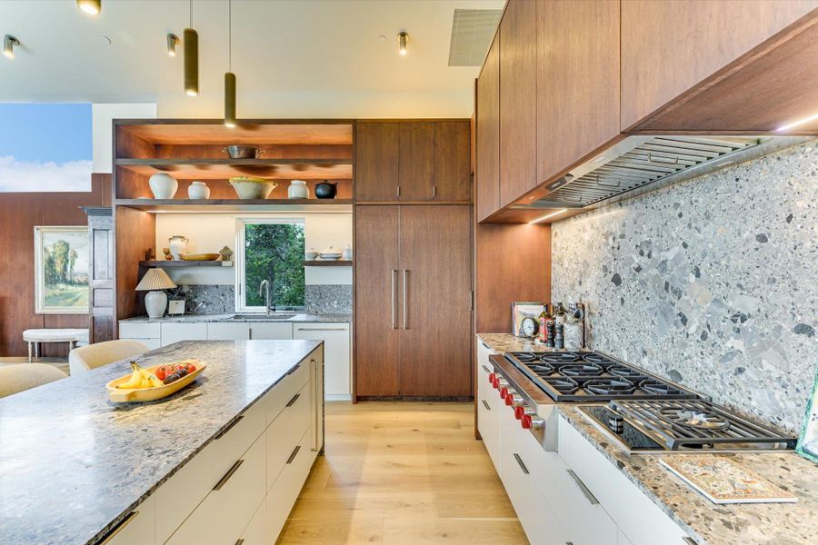 Kitchen with light stone counters, modern cabinets, open shelves, light wood finished floors, and decorative light fixtures