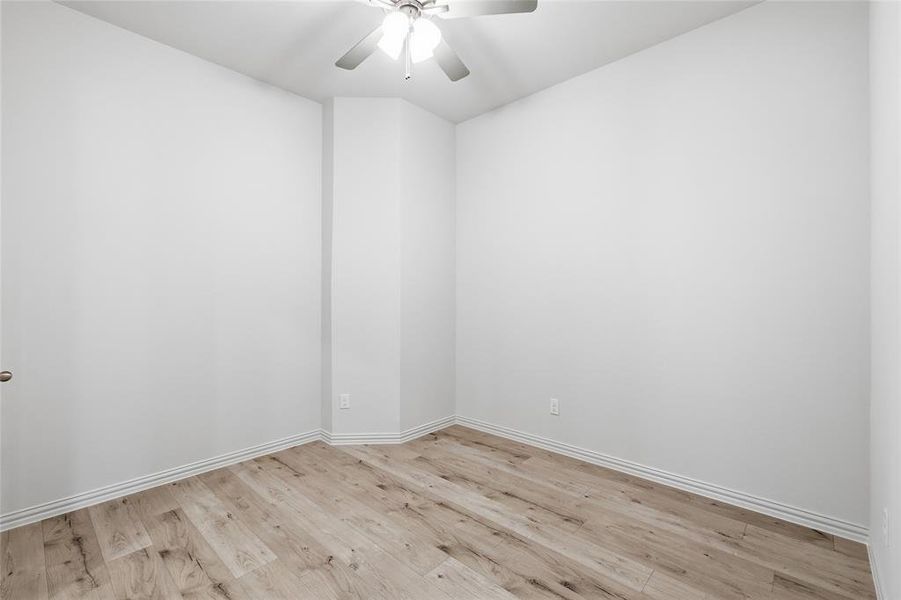 Spacious room featuring wood-finish flooring, white baseboards, and a ceiling fan with integrated lighting Spacious room featuring wood-finish flooring, white baseboards, and a ceiling fan with integrated lighting