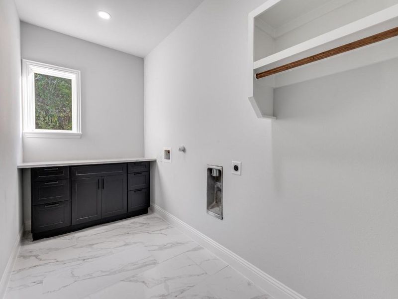 Washroom featuring electric hookup for a dryer and washing machine, light marble finish flooring.