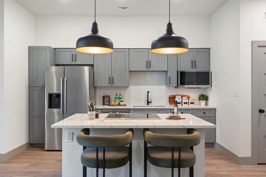 Kitchen featuring gray cabinets, stainless steel appliances, pendant lighting, light stone counters, and a kitchen breakfast bar