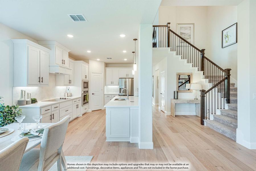Open-concept kitchen with white cabinets, center island, and staircase with dark wood railing visible nearby