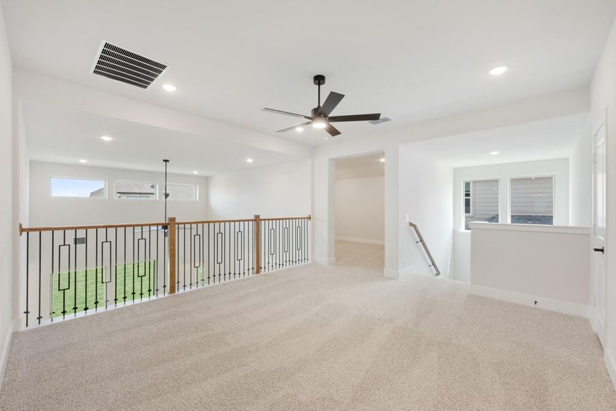 Open upstairs loft with carpet, ceiling fan, and iron stair railing overlooking lower level