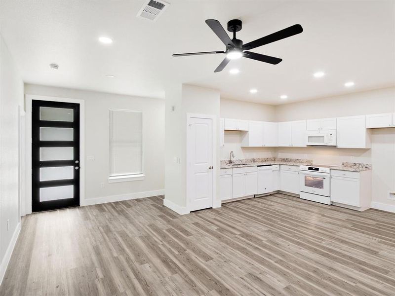 Open-concept living space with wood-finish flooring, a contemporary black entry door with frosted glass panels, and a modern ceiling fan with integrated lighting Open-concept living space with wood-finish flooring, a contemporary black entry door with frosted glass panels, and a modern ceiling fan with integrated lighting