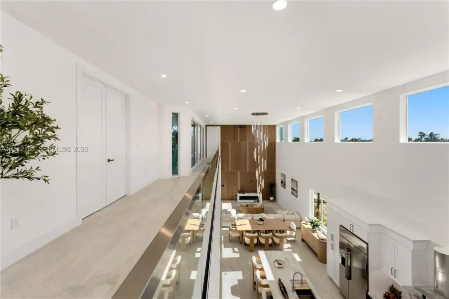 Elevated walkway featuring a sleek glass railing, wood-finish flooring, soaring ceilings, clerestory windows, and a multi-tiered modern chandelier Elevated walkway featuring a sleek glass railing, wood-finish flooring, soaring ceilings, clerestory windows, and a multi-tiered modern chandelier