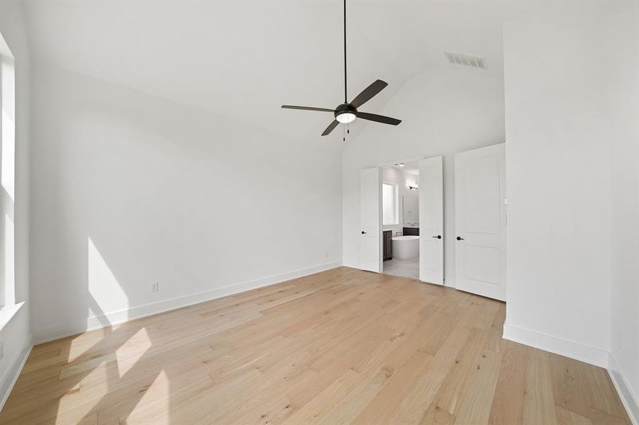 Unfurnished bedroom featuring light wood-style floors, high vaulted ceiling, ceiling fan, and ensuite bathroom Unfurnished bedroom featuring light wood-style floors, high vaulted ceiling, ceiling fan, and ensuite bathroom