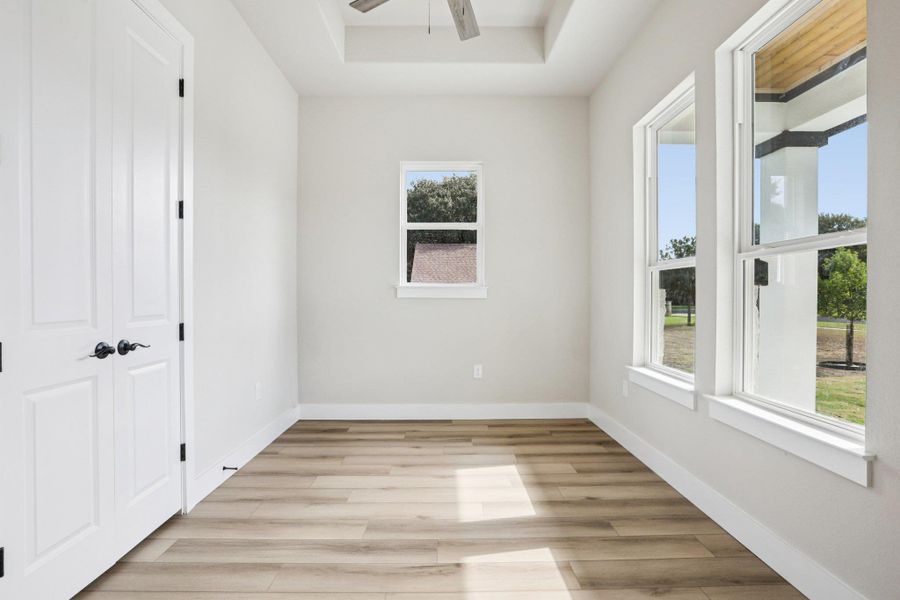 Empty room with light wood-style flooring, ceiling fan, and a raised ceiling