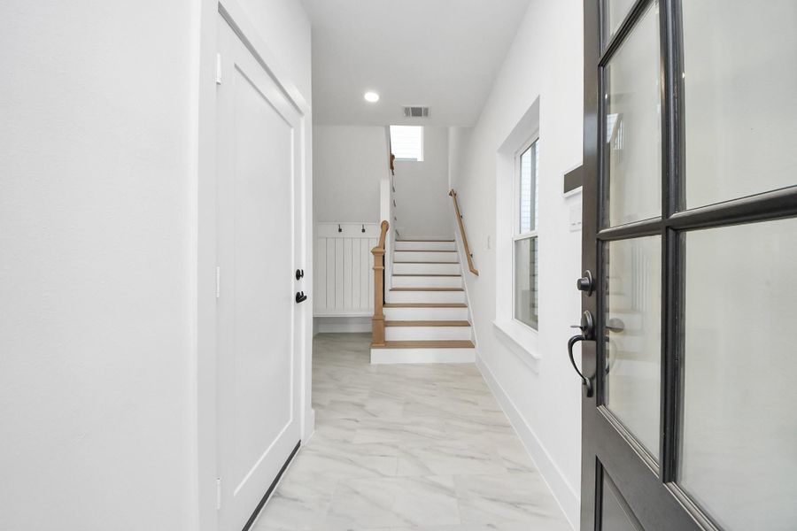 Enter thru the front door to begreeted by bright, clean entry way with a staircase leading up. The space features modern finishes with a tiled floor, natural light from a window, and a welcoming, neutral color palette.