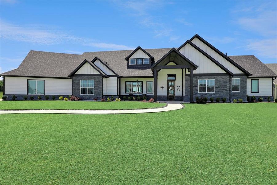 View of front of home with stone siding, roof with shingles, a front lawn, and board and batten siding View of front of home with stone siding, roof with shingles, a front lawn, and board and batten siding