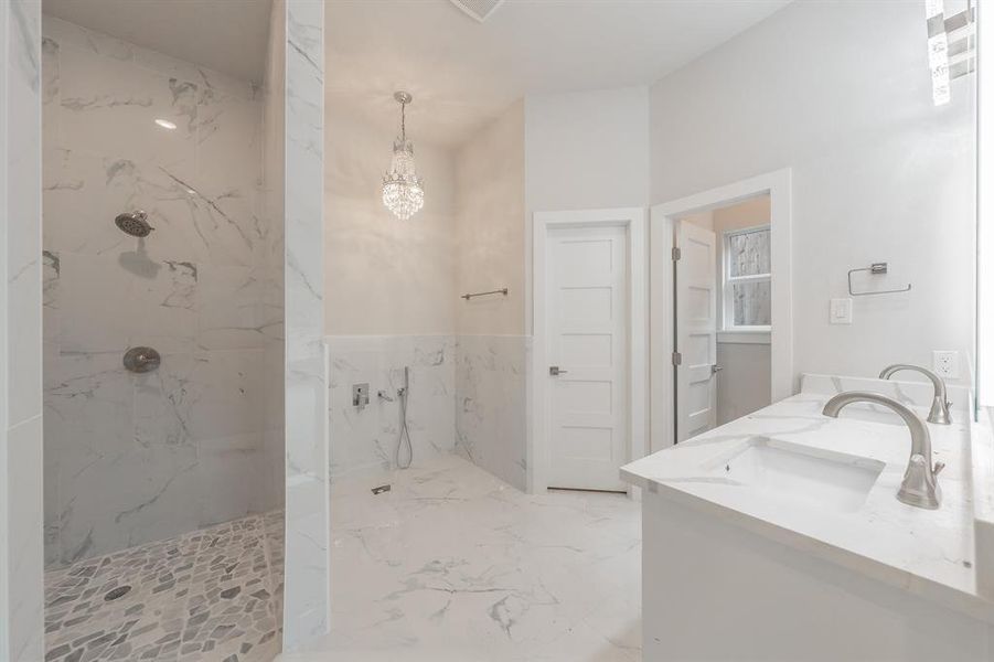 Bathroom featuring double vanity, marble tiled floors, a marble finish shower, a chandelier, and tile walls