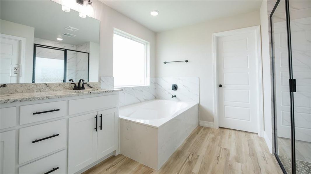 Full bathroom featuring a bath, vanity, a marble finish shower, and wood finished floors Full bathroom featuring a bath, vanity, a marble finish shower, and wood finished floors