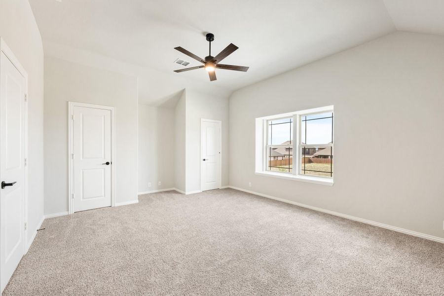 Empty bedroom with carpet, vaulted ceiling, ceiling fan, and two white doors Empty bedroom with carpet, vaulted ceiling, ceiling fan, and two white doors