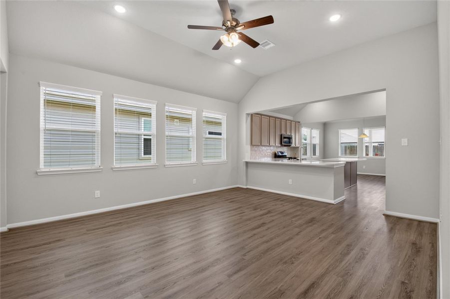 Spacious living area with high ceilings, neutral walls, and wood-look flooring. Features a ceiling fan and ample natural light from adjacent windows. Spacious living area with high ceilings, neutral walls, and wood-look flooring. Features a ceiling fan and ample natural light from adjacent windows.