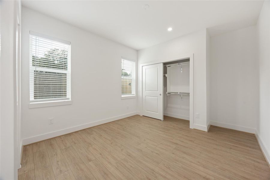 This first-floor bedroom offers a bright, versatile space with two windows, recessed lighting, wood-look flooring, and a generous closet with built-in shelving and hanging space. Ideal as a guest suite, private office, or secondary bedroom, it provides comfort and flexibility on the entry level.