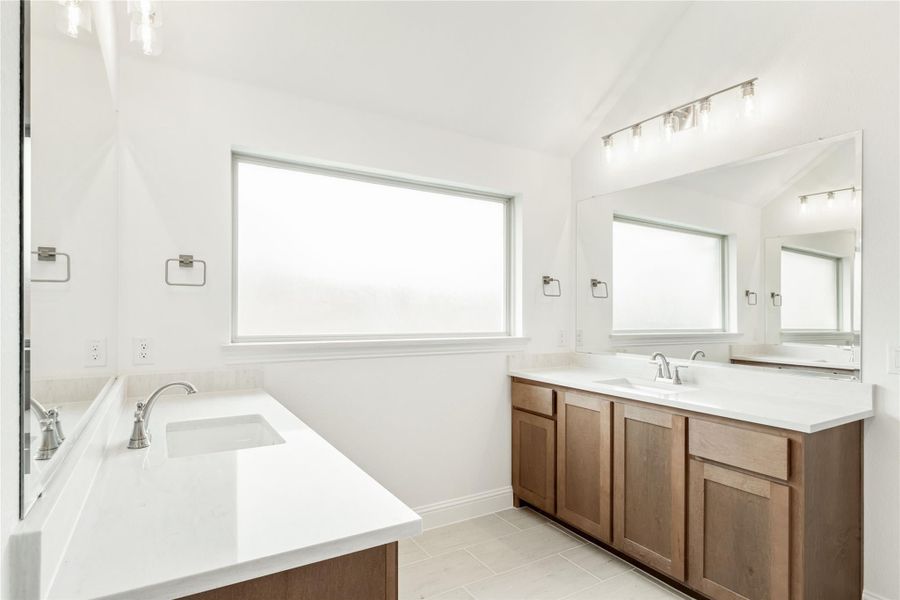 Master bathroom with dual sinks, wood cabinets, white countertops, soaking tub, and large mirror with vanity lights