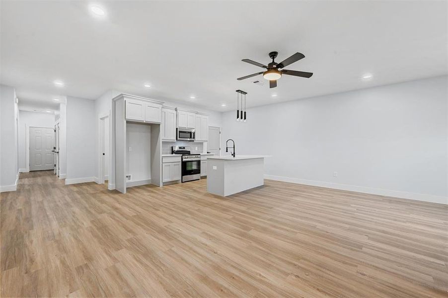 Kitchen featuring white cabinetry, sink, hanging light fixtures, a kitchen island with sink, and appliances with stainless steel finishes