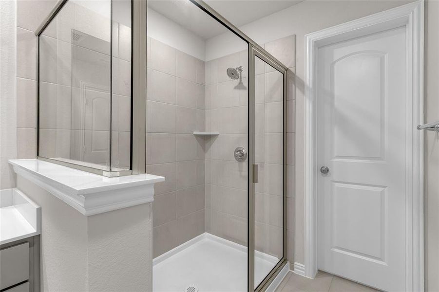 The photo showcases a modern, clean-lined bathroom with a walk-in shower enclosed by glass doors, neutral tile walls.