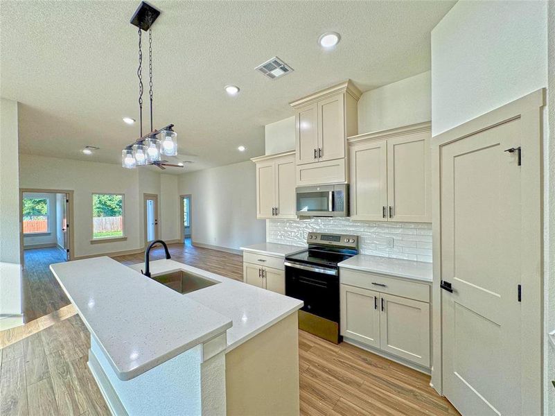 Kitchen with stainless steel appliances, a kitchen island with sink, pendant lighting, light stone counters, and backsplash Kitchen with stainless steel appliances, a kitchen island with sink, pendant lighting, light stone counters, and backsplash