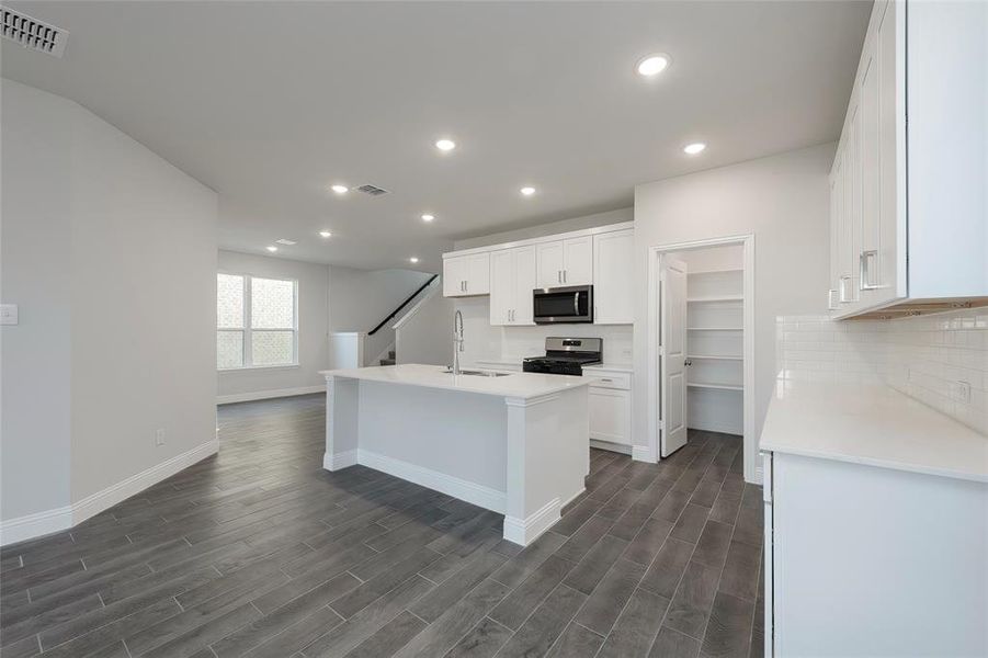 Kitchen with appliances with stainless steel finishes, baseboards, dark wood-style floors, white cabinets, and recessed lighting Kitchen with appliances with stainless steel finishes, baseboards, dark wood-style floors, white cabinets, and recessed lighting