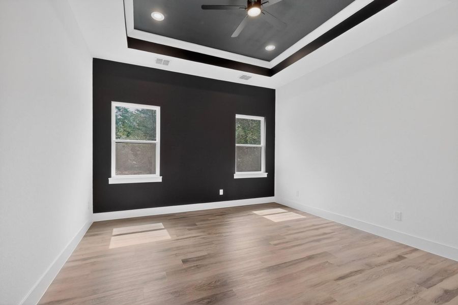 Recessed lighting illuminates the stylish tray ceiling, enhancing the bedroom's modern appeal.